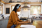 Young focused mixed race businesswoman going through paper and bills while working on a laptop at home. One hispanic female businessperson typing on a laptop and listening to music while working from home