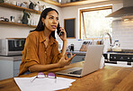 Young serious mixed race businesswoman going through paper and bills while on a call using her phone and working on a laptop at home. One hispanic female businessperson using a laptop and talking on a phone while planning her business