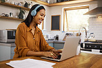 Young cheerful mixed race businesswoman going through paper and bills while typing on a laptop at home. Cheerful hispanic female businessperson typing an email on a laptop and listening to music while working from home