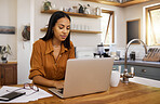 Young content mixed race businesswoman going through paper and bills while typing on a laptop at home. Serious hispanic female businessperson typing an email on a laptop while working from home