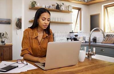 Young content mixed race businesswoman going through paper and bills while typing on a laptop at home. Serious hispanic female businessperson typing an email on a laptop while working from home