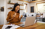Joyful mixed race businesswoman cheering with joy while going through paper and bills and working on a laptop at home. Cheerful hispanic female businessperson cheering with excitement while working from home
