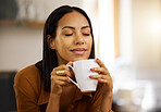 Young happy beautiful mixed race woman enjoying a cup of coffee alone at home. Hispanic female in her 20s smiling while drinking a cup of tea in the kitchen at home