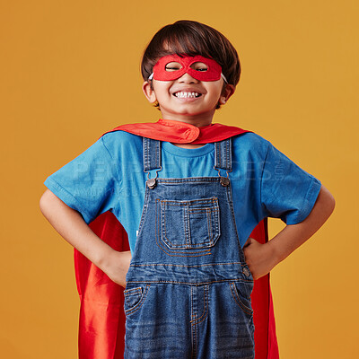 Adorable little asian boy wearing a mask and a cape while pretending to be a superhero against an orange studio background. Cute happy boy pretending to be a character for halloween