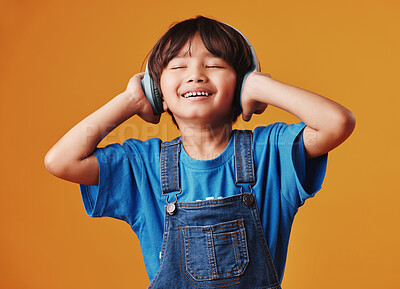 A cute little asian boy enjoying listening to music while wearing headphones against an orange copyspace background .Adorable Chinese kid feeling the magic of music