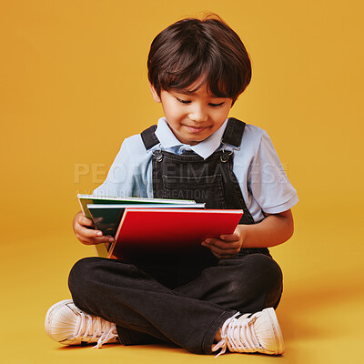 One cute little asian boy sitting on the floor wearing casual clothes while reading against an orange background. Happy and content while focused on education. Child ready for school
