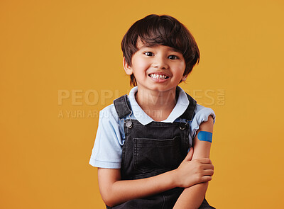 Portrait of a smiling happy mixed race showing his bandaid and posing against an orange copyspace background after getting the Covid vaccine injection. Happy child after getting his shots