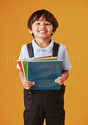 Portrait of a cute little asian boy wearing casual clothes while reading against an orange background. Happy and content while focused on education. Child holding a stack of books