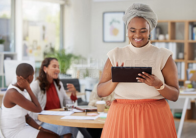 Smiling african american business woman using a digital tablet while colleagues sit behind her in office. Ambitious and happy black professional standing and holding technology while browsing schedule