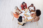 Above view of diverse group of business women having a brainstorm meeting in office with copyspace. Confident professional team sitting together and using paperwork while planning a marketing strategy