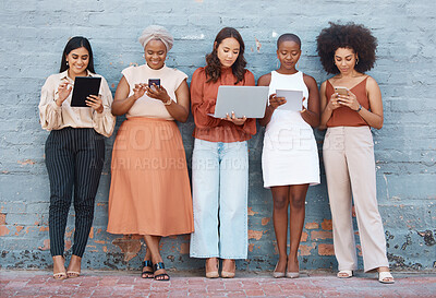 Group of five young happy cheerful businesswomen standing against a wall outside in the city and using tech. Happy colleagues using technology and standing in a line outdoors