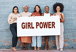 Group of five diverse young businesswomen standing against a wall holding a girl power sign outside in the city. Team of colleagues holding a sign with a message while standing in a row together outdoors