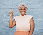 One happy african american woman wearing a turban and smiling while showing the peace sign with her hand and standing outside against a brick wall