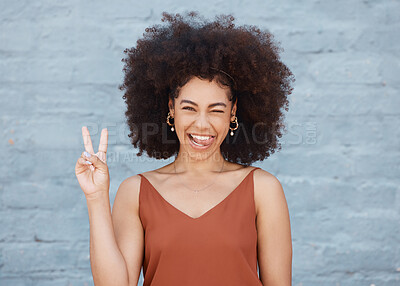 One young mixed race business woman with an afro standing outside against a grey wall and gesturing the peace sign with her hand. Happy and confident female executive looking positive and carefree