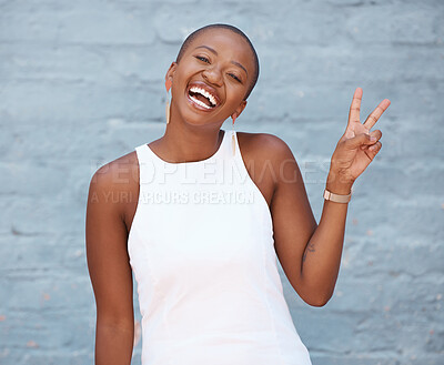 Young african american woman showing a peace sign with her hand smiling and looking happy while standing against a grey wall outside in the city. Peace, love and unity