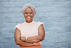 One smiling African American businesswoman with headscarf posing with arms crossed against a grey background. Portrait of confident, successful, powerful black woman against wall. Females in business