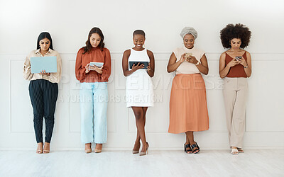 Group of five young happy cheerful businesswomen standing against a wall in an office and using tech. Happy colleagues using technology and standing in a row together at work