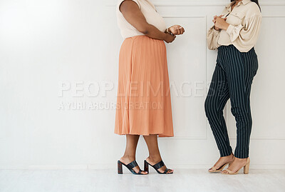 Two formal businesswoman standing against a wall and talking in an office at work. Legs of businesspeople having a meeting and planning together