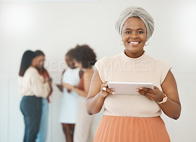 Portrait of a young content african american businesswoman holding and using a digital tablet standing in an office at work. Black woman smiling while using social media on a digital tablet
