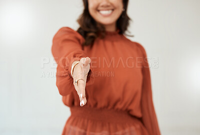 A unrecognizable mixed race woman reaching out and greeting while making a handshake gesture with her hand and smiling against a grey studio background. Welcome it\'s so nice to meet you