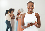 Portrait of a young happy african american businesswoman holding and using a digital tablet standing in an office at work. Black female businessperson smiling while using social media on a digital tablet