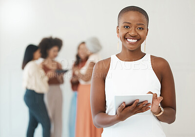 Portrait of a young happy african american businesswoman holding and using a digital tablet standing in an office at work. Black female businessperson smiling while using social media on a digital tablet
