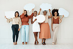Group of five diverse young businesswomen standing against a wall in an office and holding speech bubbles. Happy colleagues holding blank boards while standing in a row together at work