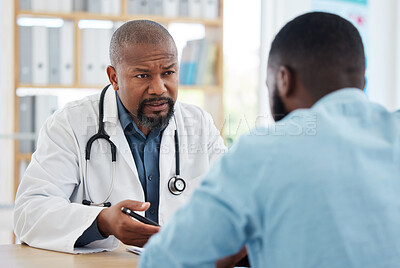 Serious doctor having a consult with a patient. Medical doctor talking to a patient about his results. African american patient speaking to his doctor in a clinic. Doctor and patient in a checkup