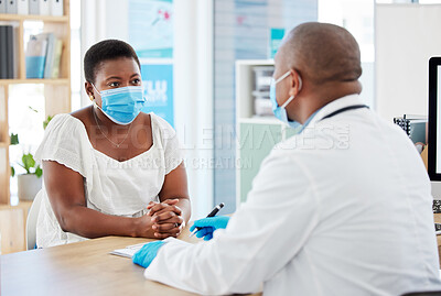 Young woman talking to her doctor about her covid results. African american woman wearing a mask during a medical checkup. Caring gp talking to patient about their test results on a clipboard
