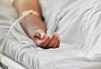 Closeup shot of the hand of an african american man lying in a hospital bed inside of a ward. Mixed race male patient with an IV drip inserted into his arm and receiving treatment and care at a clinic