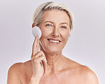 Portrait of a  mature caucasian woman using a cotton pad to remove makeup during a selfcare grooming routine. Older model  applying cleanser to her face against pink copyspace background