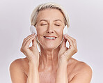 A mature caucasian woman using a cotton pad to remove makeup during a selfcare grooming routine. Older model  applying cleanser to her face against pink copyspace background