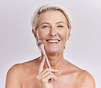 Portrait of a smiling mature caucasian woman posing with a makeup brush during a pamper routine. Older model holding a contouring brush against a purple copyspace background