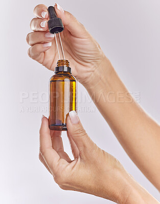 Closeup of unknown caucasian woman isolated against a grey studio background holding a bottle of skin, face serum with a dropper. Models hands promoting essential oil in a studio