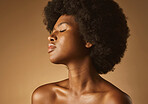 Confident African American woman with a natural afro posing against brown studio copyspace background. Young beautiful black female model looking trendy, powerful and sensual with smooth glowing skin