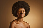 Portrait of one beautiful african american woman with an afro and flawless skin posing topless in a studio. Powerful, exotic black woman with glowing skin touching her face with her hand. Healthy skin