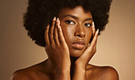 Portrait of one beautiful african american woman with afro posing in a studio and touching her face with her hand. Exotic and powerful black woman feeling confident and showing flawless, healthy skin