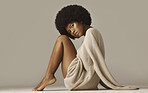 Beautiful african american woman with afro wearing casual winter sweater and sitting barefoot and knees up. Attractive female with glowing skin wearing warm and cozy knitwear against brown background