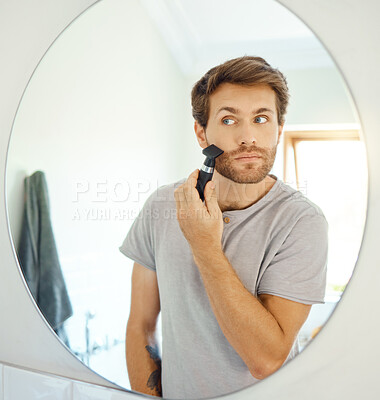 Buy stock photo Mirror, grooming and a man shaving in the bathroom of a home in the morning for personal hygiene. Electric razor, reflection and morning routine with a young male person in his home for hair removal