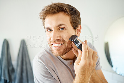Buy stock photo One handsome man shaving his face hair in a bathroom at home. Caucasian male using a shaver while looking in a mirror in his apartment