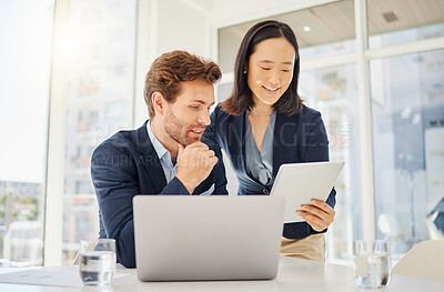 Two happy young diverse colleagues working together on a digital tablet in an office. Confident asian businesswoman showing smiling caucasian businessman corporate plans and ideas on device. Secretary assisting boss at work