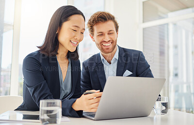 Two happy young diverse colleagues working together on a laptop in an office boardroom. Confident asian businesswoman explaining corporate plans and ideas to smiling caucasian businessman during a meeting