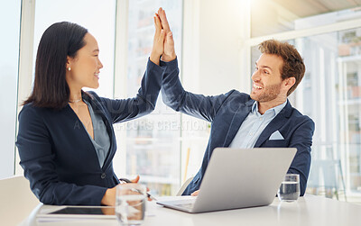 Two happy young diverse colleagues giving each other a high five while working together on a laptop in an office. Excited caucasian businessman celebrating a winning success with motivated asian businesswoman
