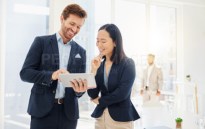Two happy young diverse colleagues discussing plans and ideas together on a digital tablet device in an office. Asian businesswoman and caucasian businessman brainstorming online with smart apps
