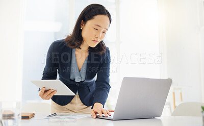 Focused young asian businesswoman using a digital tablet device and laptop while planning notes at a desk in an office. One female only browsing online while planning research documents and reviewing data. Lawyer compiling legal reports