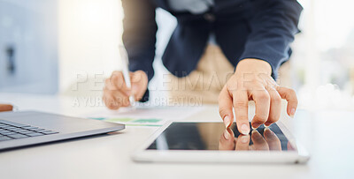 Closeup of one businesswoman writing notes while using a digital tablet and laptop at a desk in an office. Hands of female entrepreneur touching device screen to browse online while planning research documents and reviewing reports