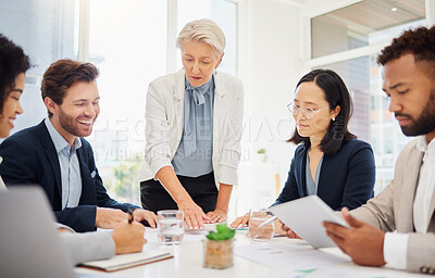 Mature caucasian businesswoman leading a presentation with her diverse colleagues during a meeting in an office boardroom. Businesspeople going through paperwork while planning a strategy together. Team brainstorming with their manager