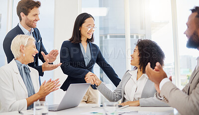 Smiling young asian and mixed race businesswomen shaking hands during a meeting in an office boardroom. Diverse businesspeople cheering and clapping hands while feeling inspired after a successful promotion, corporate deal and merger