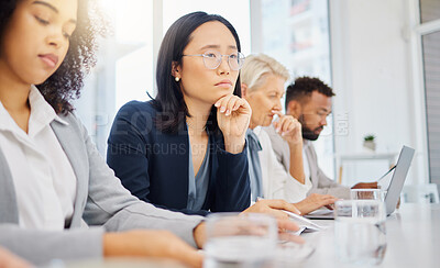 Serious young asian businesswoman wearing glasses and thinking with hand on her chin while listening to presentation meeting in an office boardroom with colleagues. Focused woman considering ideas and plans while sitting on a panel during a conference