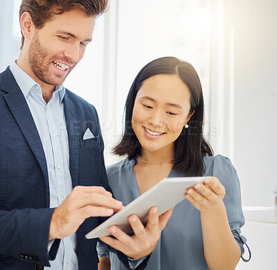Two happy young diverse colleagues working together on a digital tablet in an office. Confident asian businesswoman and smiling caucasian businessman discussing corporate plans and ideas while using apps on device